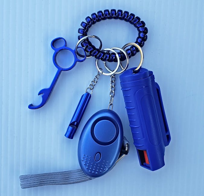 Close-up of blue personal safety items on a keychain, including a whistle and pepper spray.