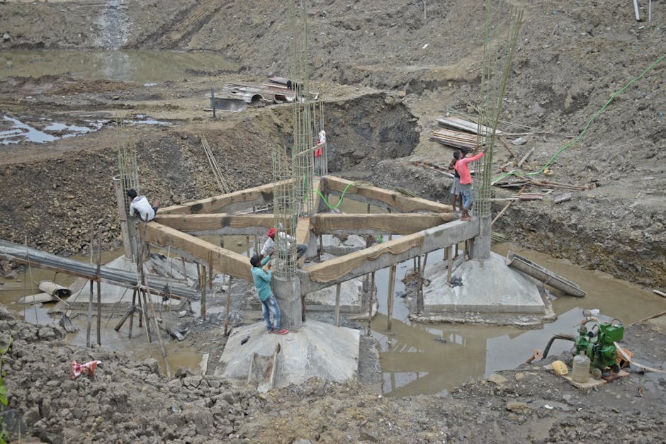 Workers constructing a building foundation with rebar and wooden supports outdoors.