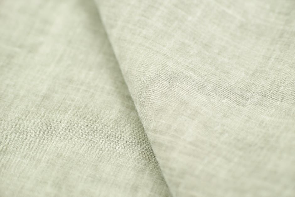 A close-up view of a soft, light-colored linen fabric displaying its intricate texture and weave.